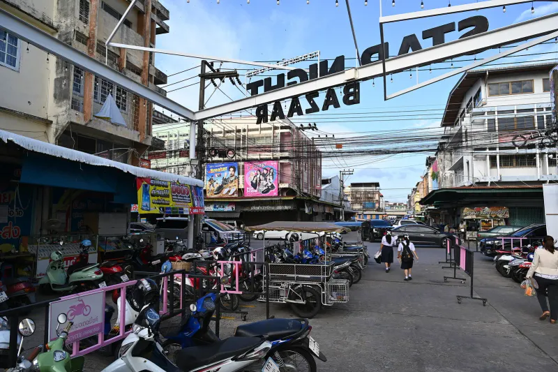 Rows of parked scooters behind pink barriers on a Thai market street in daylight