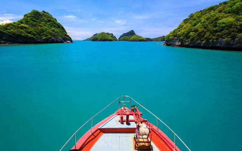 Blue-roofed ferry pier with Welcome to Koh Samui signs and forested hills behind the water