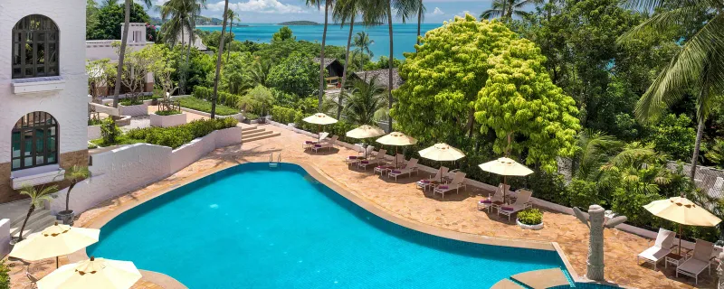 Curved blue pool with sunbeds and parasols above the bay at Sheraton Samui Resort