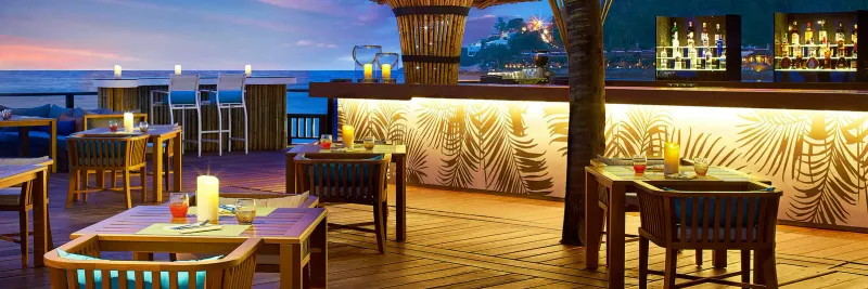 Blue Monkey beach bar terrace at dusk with candlelit tables and a palm-print bar at Sheraton Samui Resort