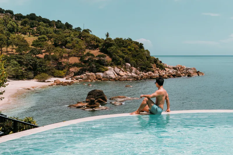 Infinity pool edge above a rocky headland and sandy cove on the Koh Samui coast