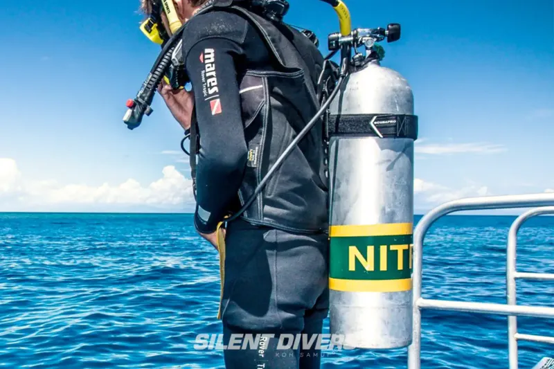 A diver in a wetsuit with a nitrox tank on a dive boat deck, with the Silent Divers watermark in the corner