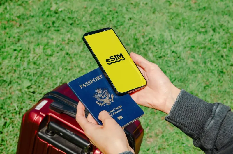 Traveler holding a smartphone with an eSIM screen next to a passport and luggage before a Thailand trip