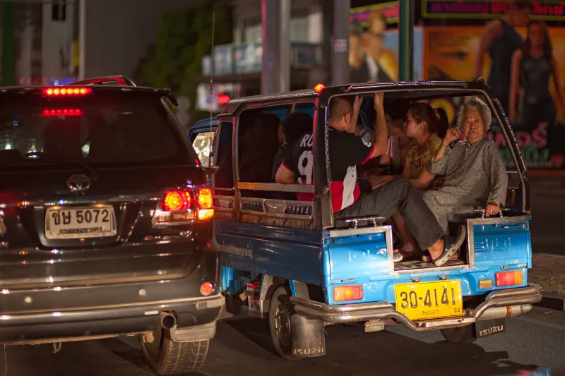 Blue songthaew pickup truck crowded with passengers in night traffic on a Thai street