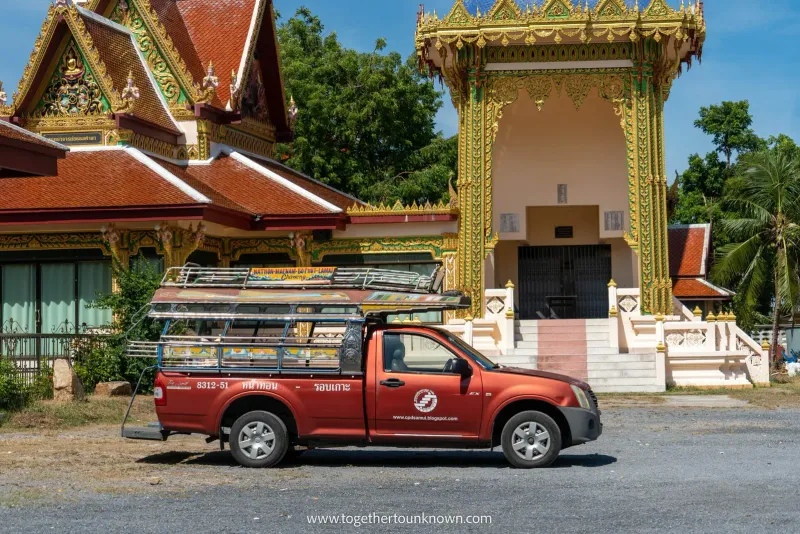 Red songthaew pickup truck with a roof rack parked in front of a Thai temple on Koh Samui