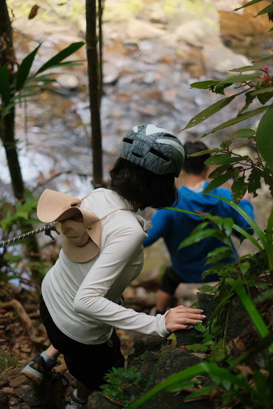Hikers scrambling up a steep, rocky jungle trail near a forest stream