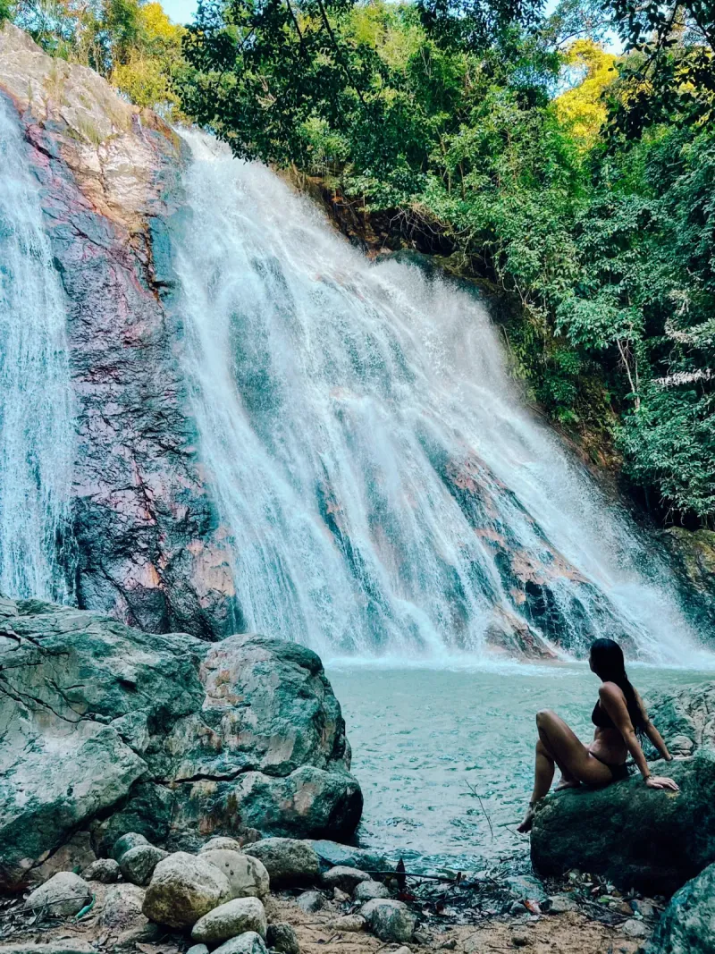 A visitor relaxing beside a cascade streaked with red mineral rock