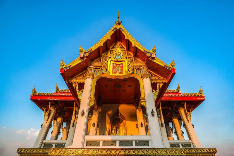 Gabled Thai temple roofline with gilded finials glowing at sunset