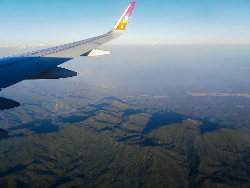 タイの国内線の窓側席から見た、森に覆われた丘の上を飛ぶ旅客機の翼