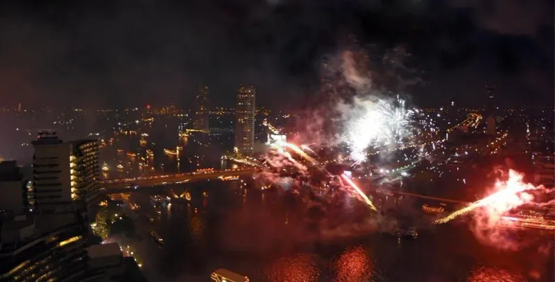 Abendliche Loy-Krathong-Feier in Thailand mit Feuerwerk und schwimmenden Kerzenflößen auf dem Wasser
