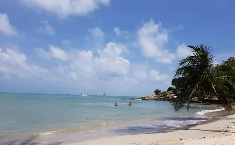 Swimmers in shallow water beside anchored boats off a quiet Koh Samui beach