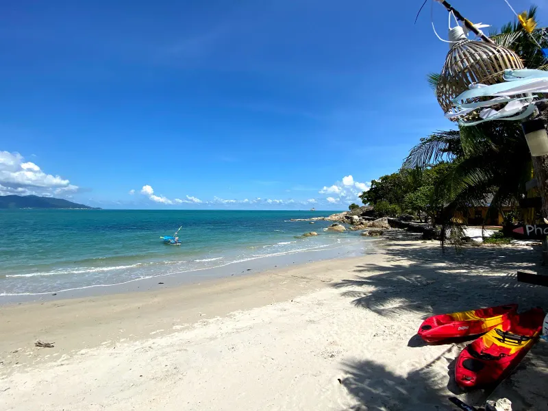 Kayaks and a longtail fishing boat resting on Thongson Bay's sand near the tree line