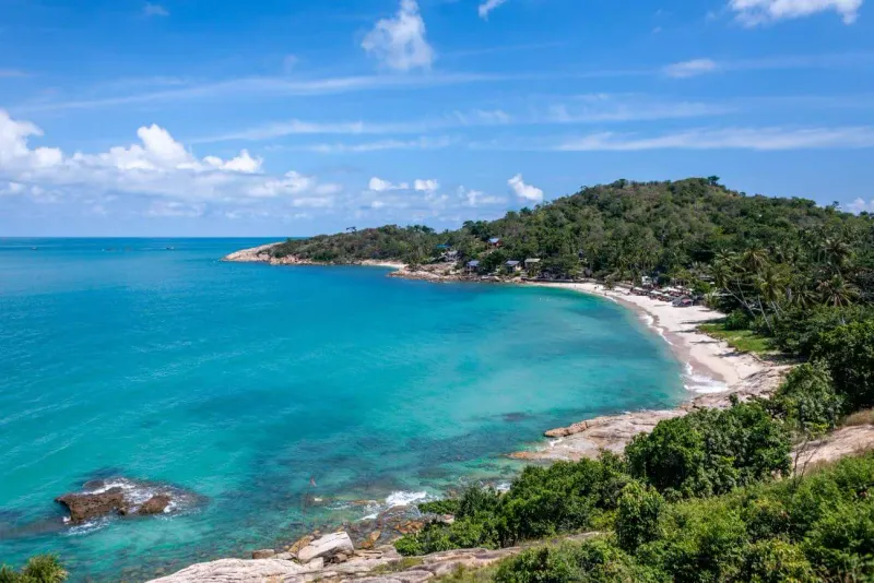 Aerial view of a crescent bay wrapped by a forested headland on Koh Samui's northeast coast