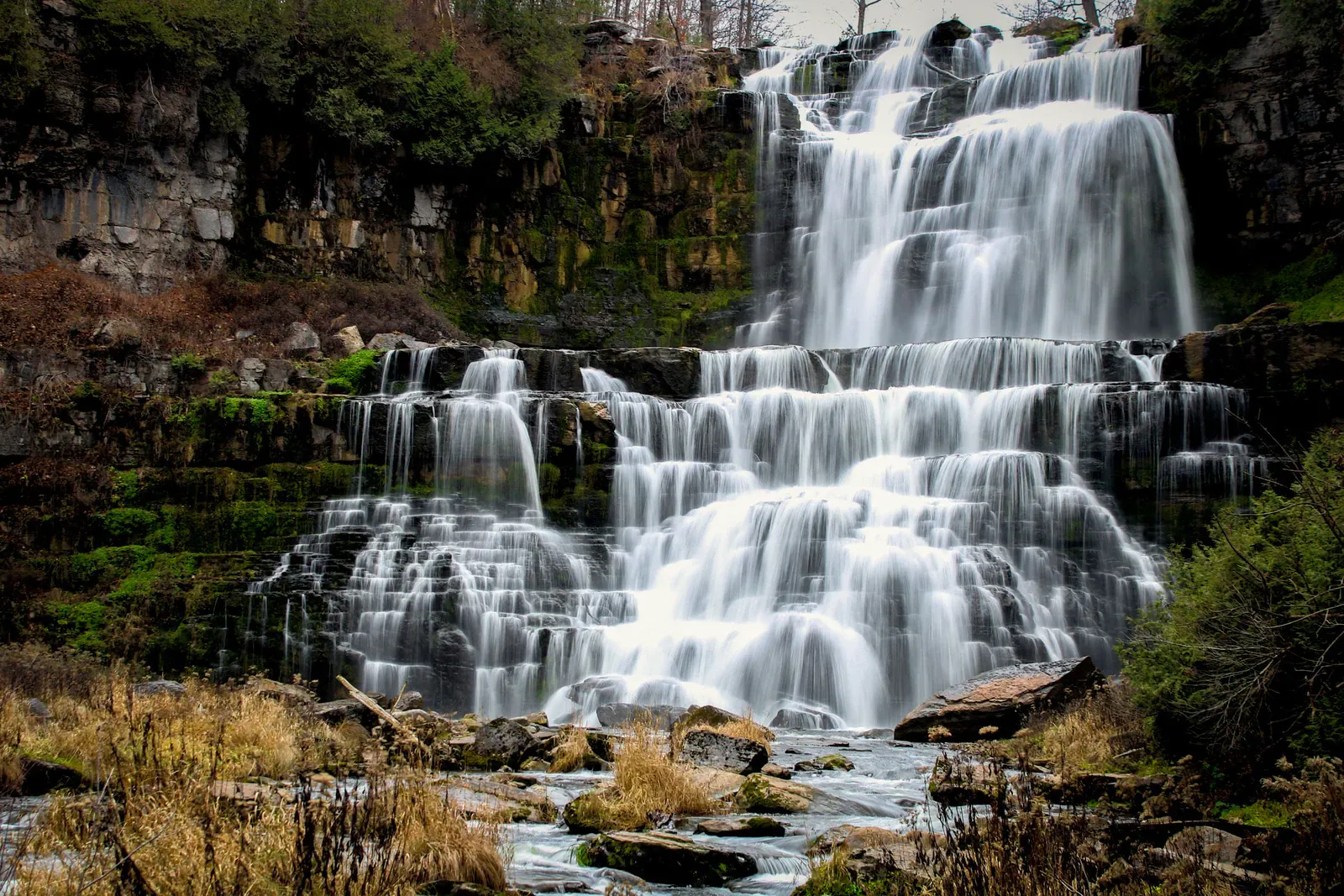 A multi-tiered waterfall cascading over moss-covered rocks in dense jungle