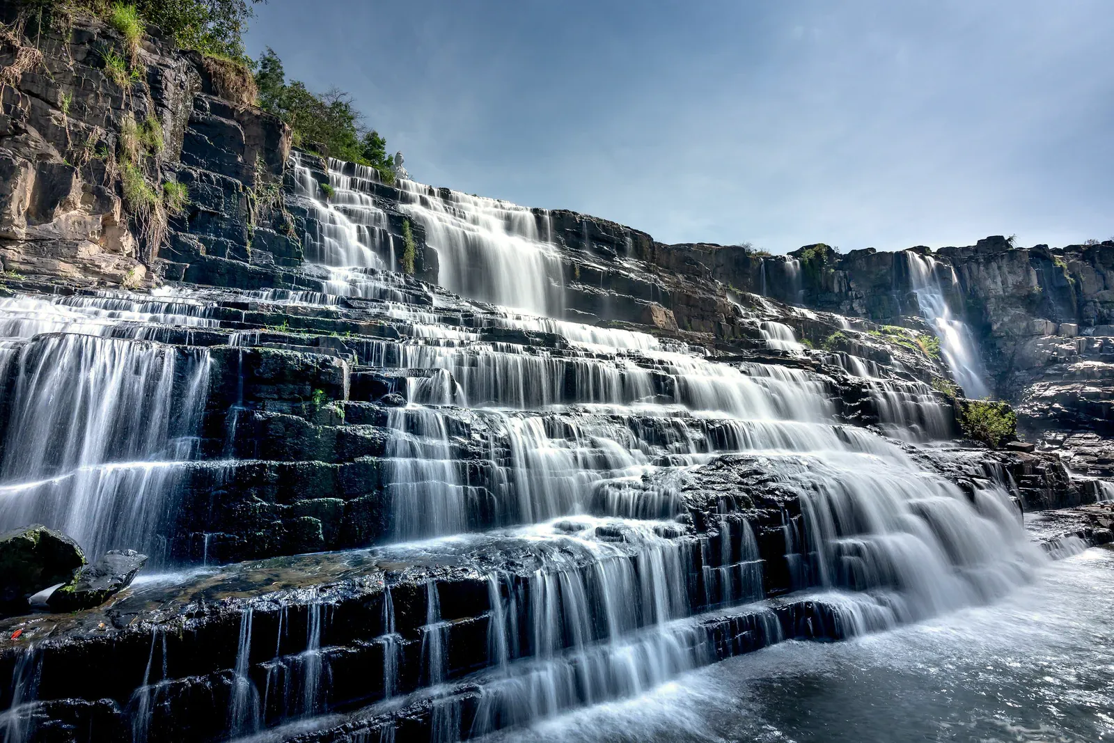 Waterfall flowing over tiered rocks under a bright sky