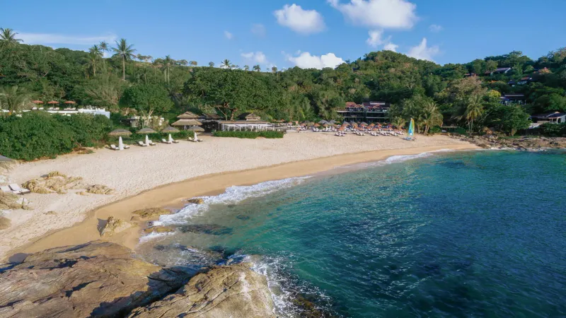 Ground-level view of Tong Sai Bay's sand and resort buildings framed by a shading tree