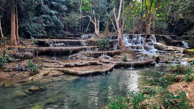 Tropical forest waterfall cascading over layered rock terraces into clear pools