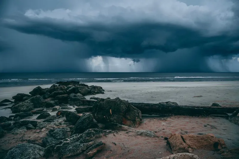 Moody storm clouds over a rocky Koh Samui coastline with driftwood on the sand during monsoon season