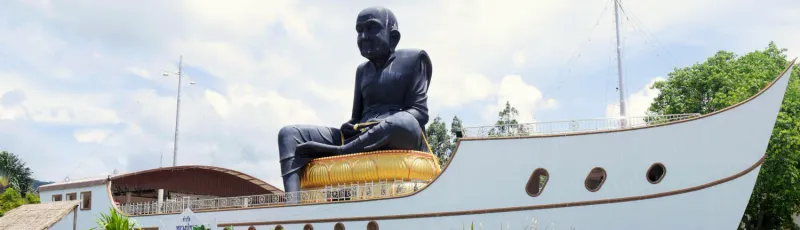 The massive black Luang Pu Thuad statue seated atop a white ship-shaped shrine